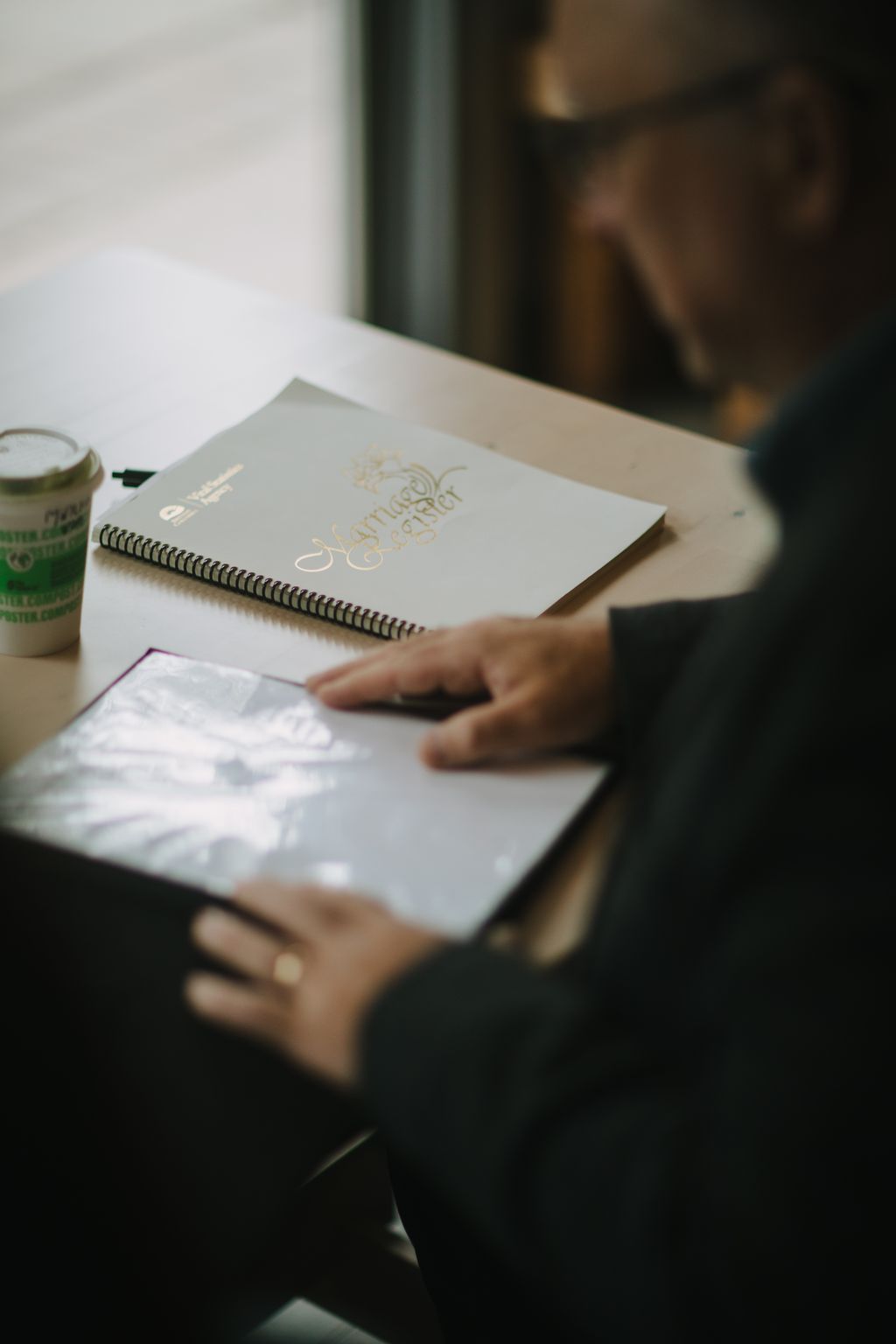 Hands hold open a spiral-bound notebook with gold lettering on its cream cover