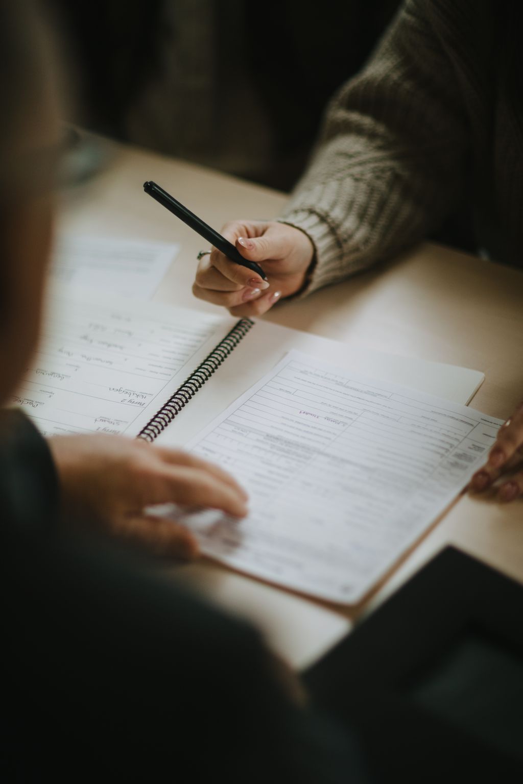 Person in knit sweater holding black pen over spiral notebook with lined pages, hand poised to write