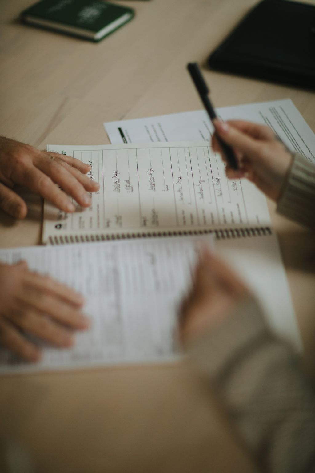 Hands holding open a spiral-bound wedding planning notebook with handwritten notes across lined pages, black pen nearby