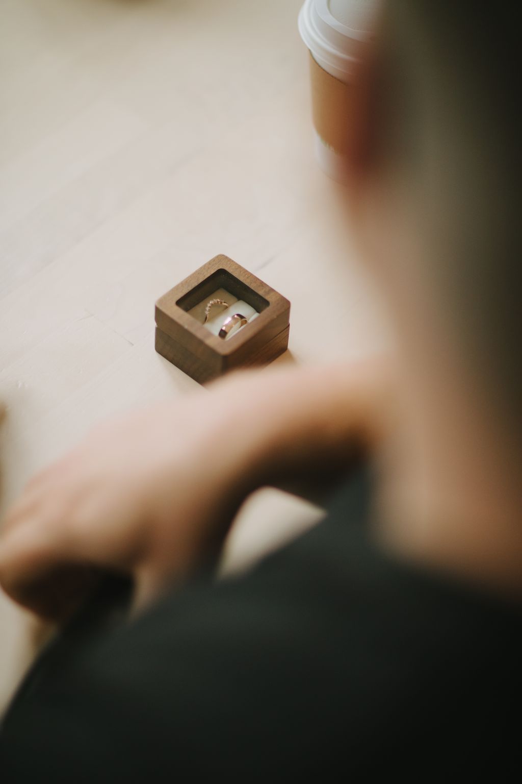 Two gold wedding bands rest in a wooden ring box, photographed from above with selective focus