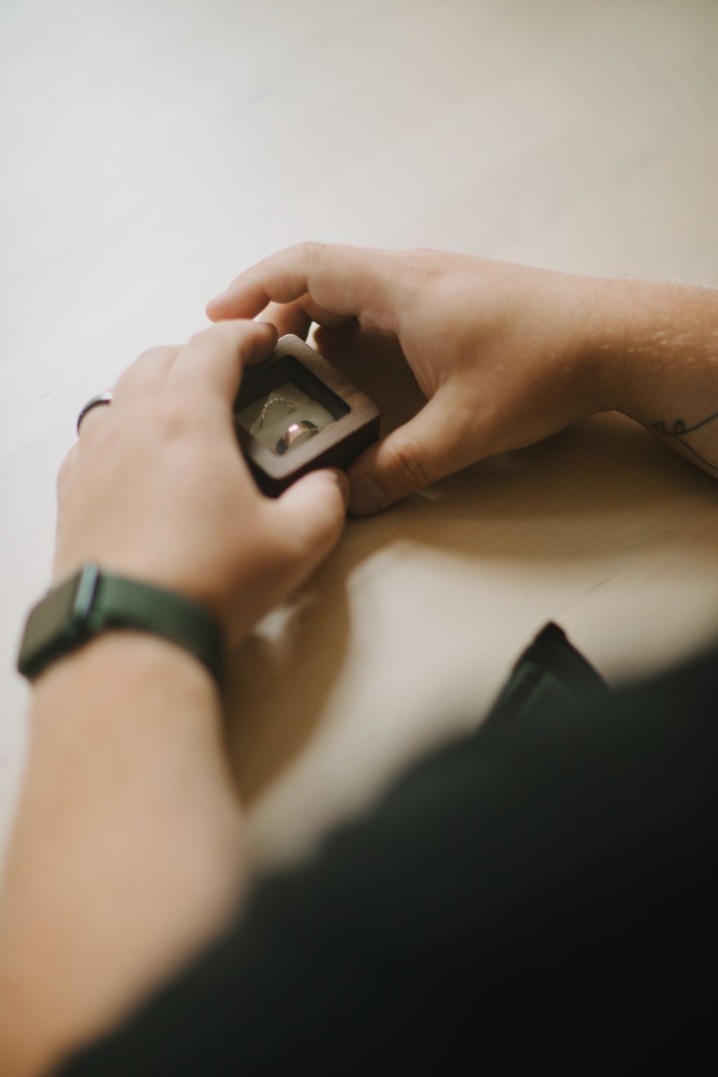 Two hands open a small wooden box to reveal a delicate ring inside, soft natural light illuminating the intimate moment