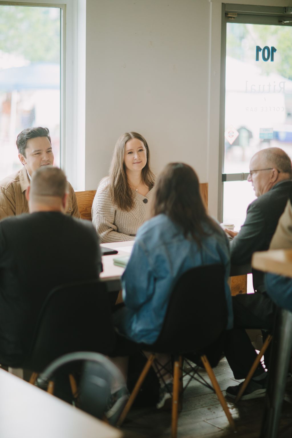 Woman in cream knit sweater smiles across table during meeting in bright, minimalist room with white walls