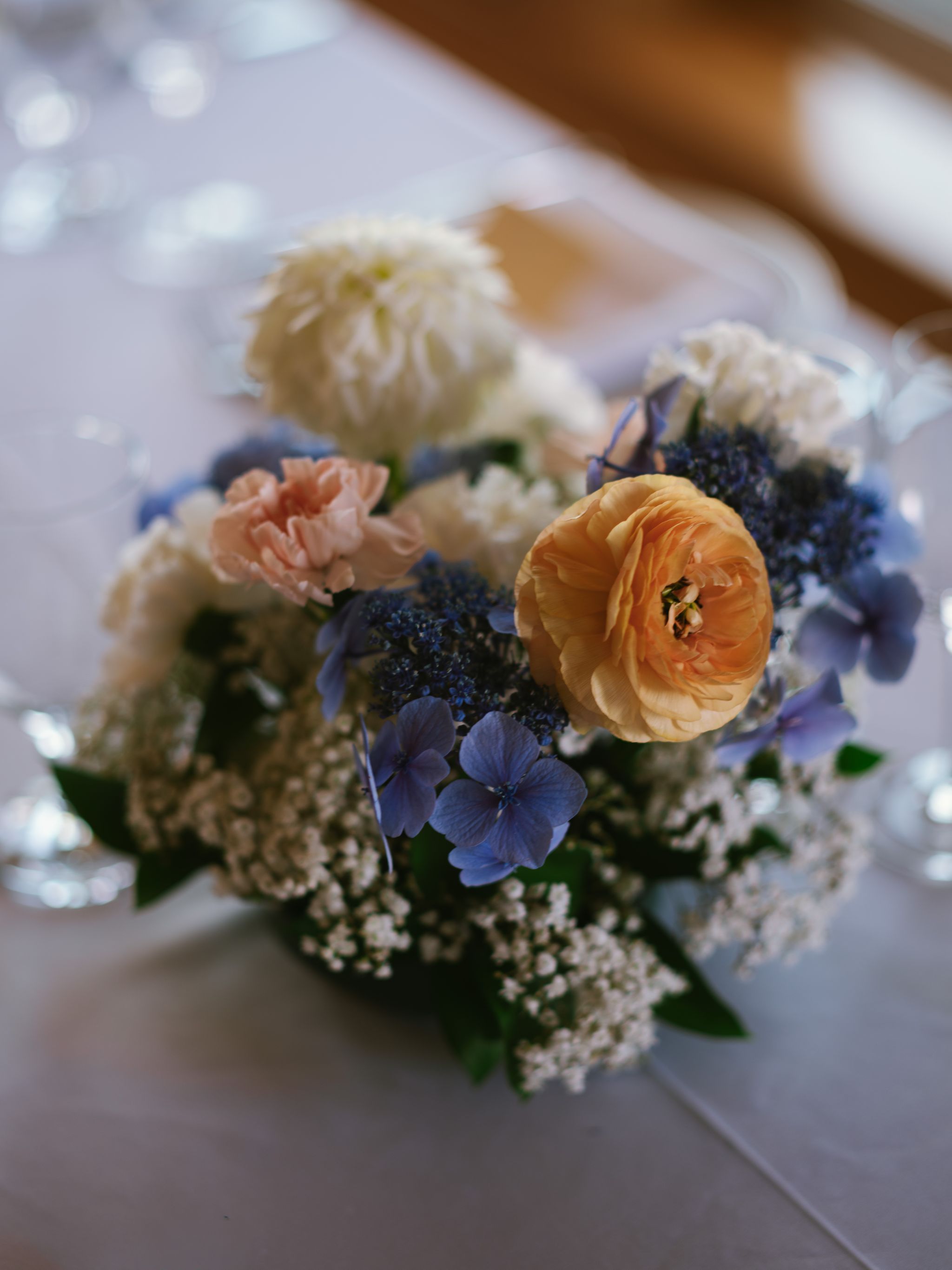 Close-up of blue hydrangea florets with peach roses and baby's breath in soft afternoon light