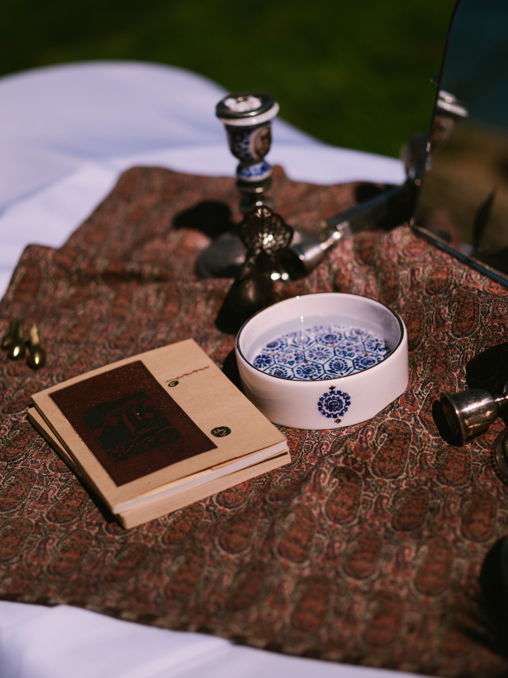 Ceramic bowl with blue pattern and antique candlestick sit on patterned textile beside cream envelope, soft natural light